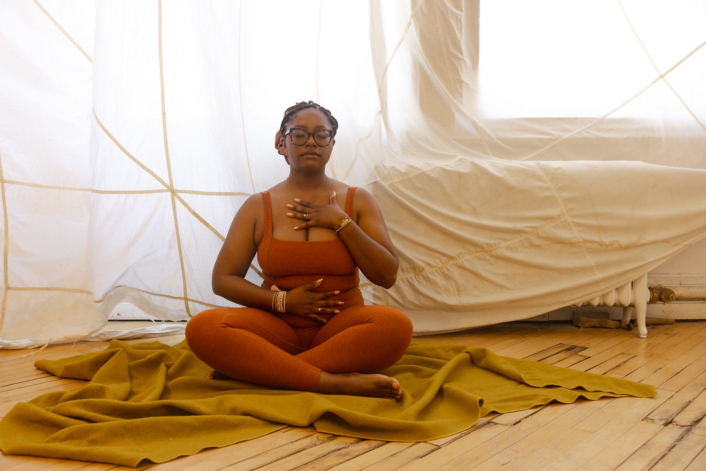 Picture of a Black woman meditating wearing orange leggings and a matching tank top