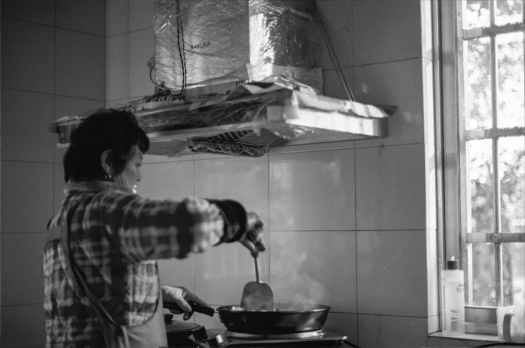 A person in a kitchen cooking food on a stove A person in a kitchen cooking food on a stove