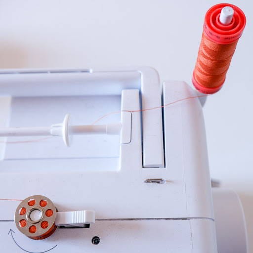 an bobbin being wound on a bobbin winder pin of a sewing machine with orange thread