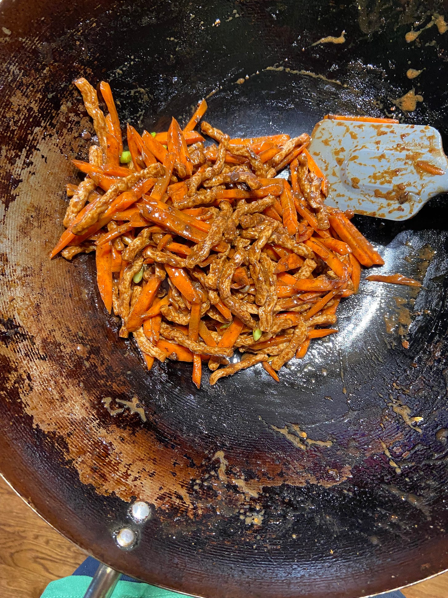 A wok with carrots and meat sticks in it. There is a spatula also in the wok.