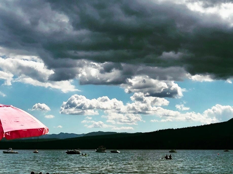 An assortment of boats on Lake Tahoe, with a large pink umbrella at the bottom left and ominous dark clouds above