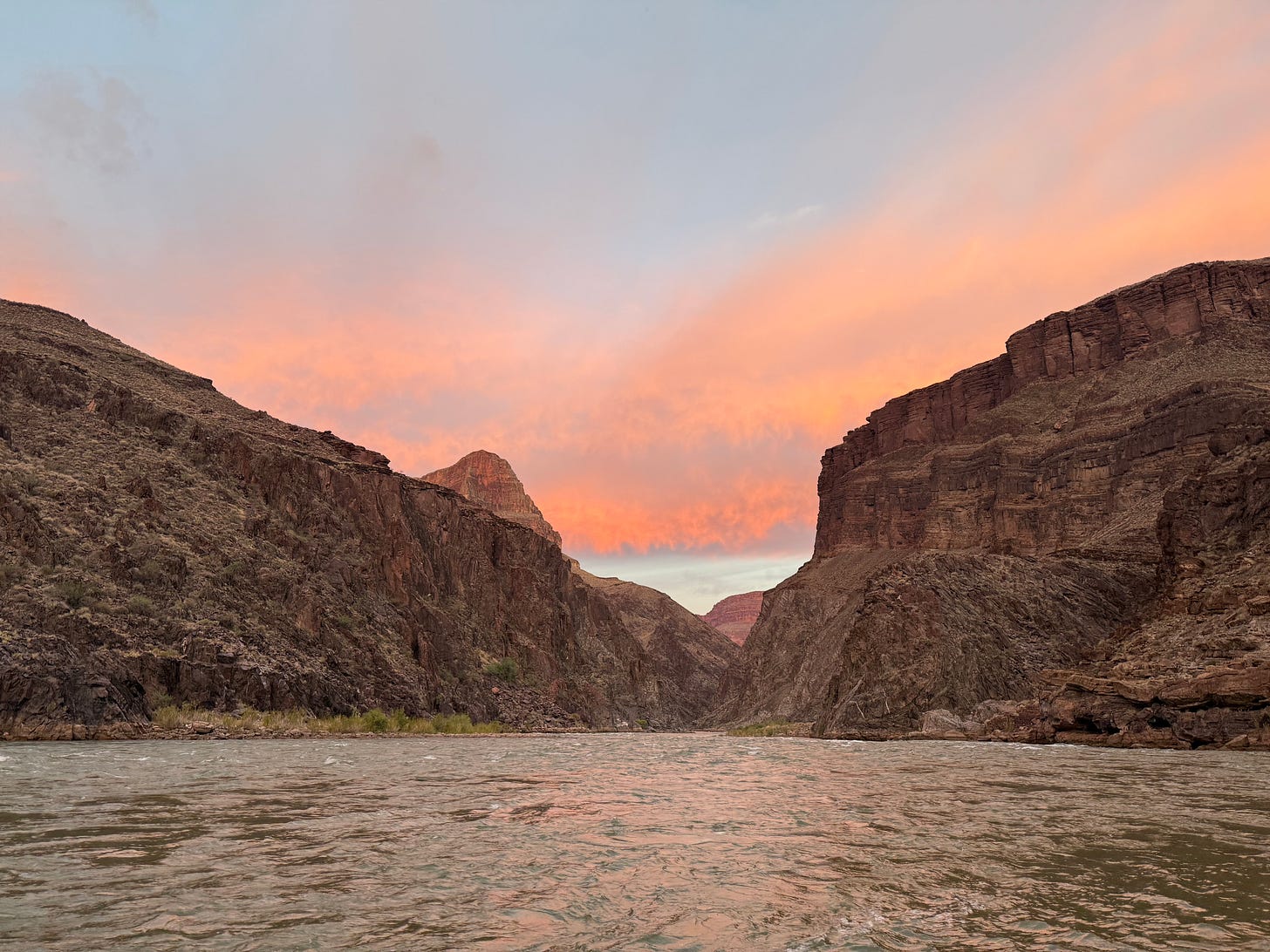 Looking downstream on a river surrounded by canyons as the sun sets.