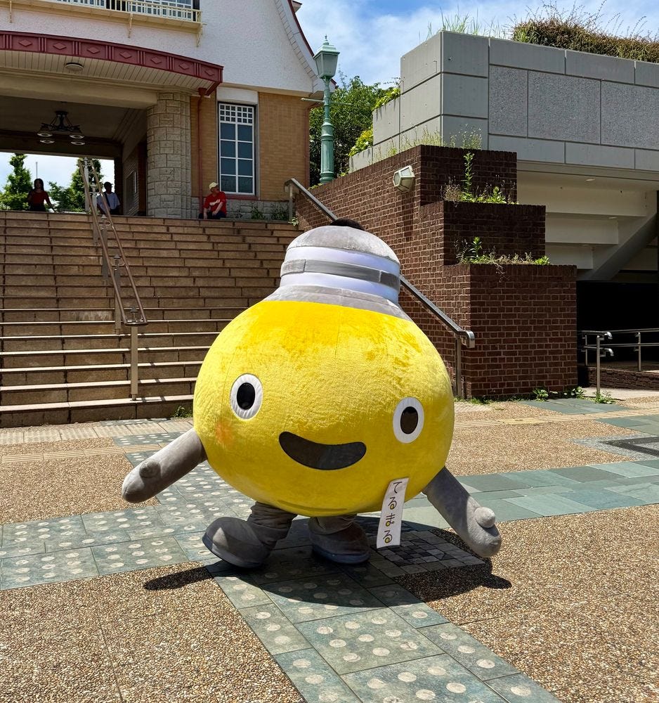 A yellow lightbulb mascot stands in a town square.