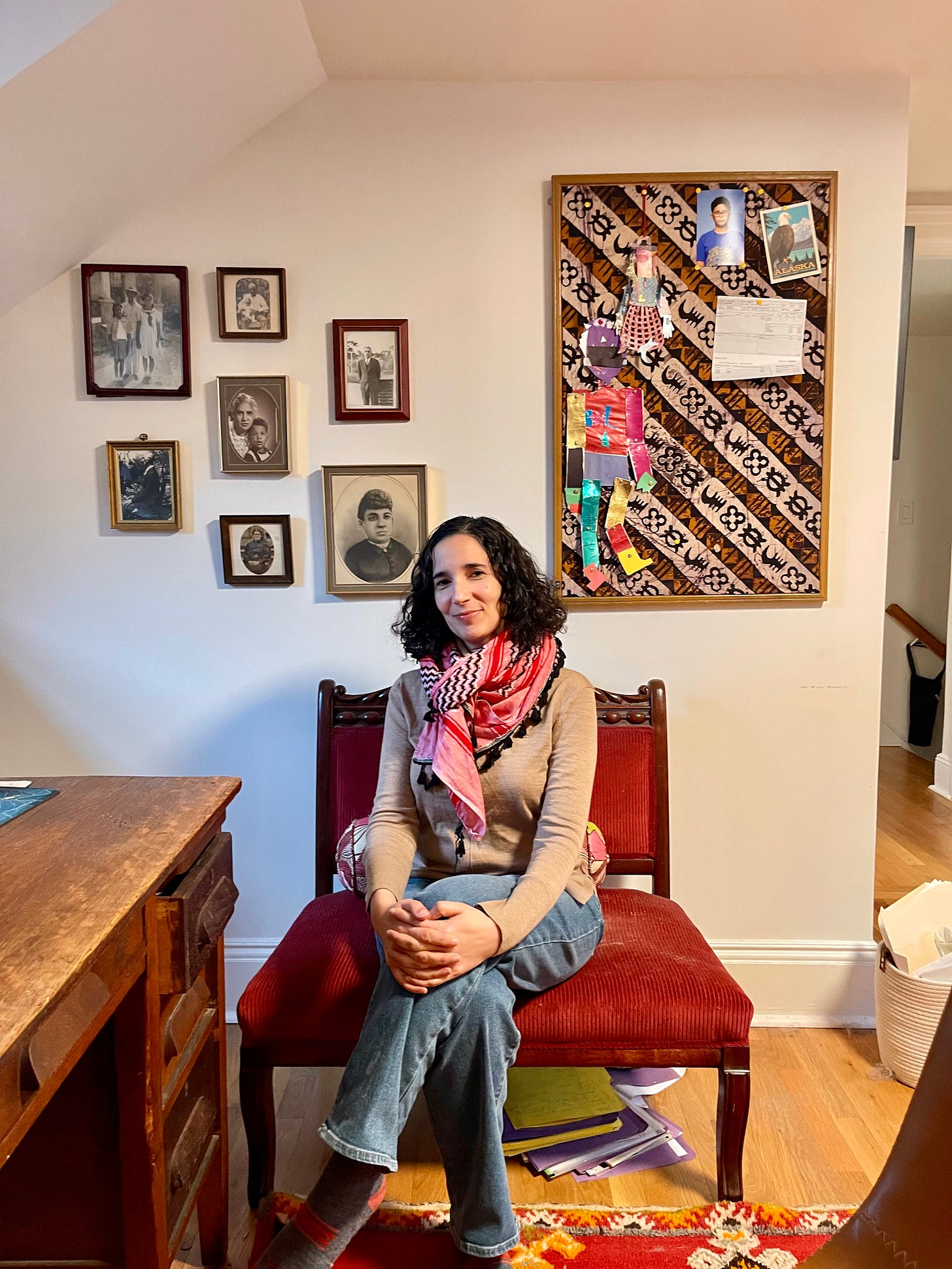 Emily Raboteau smiles from a chair in front of her ancestor wall.