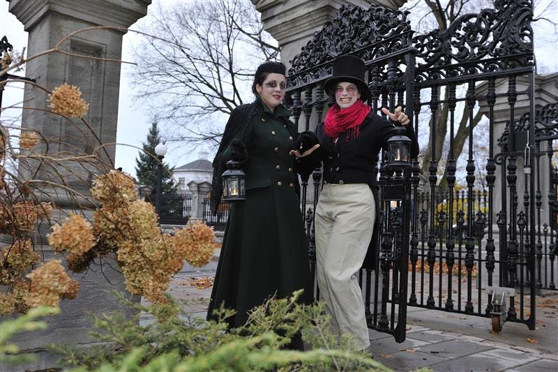 Two people in historical costumes stand at the gates of Rideau Hall.