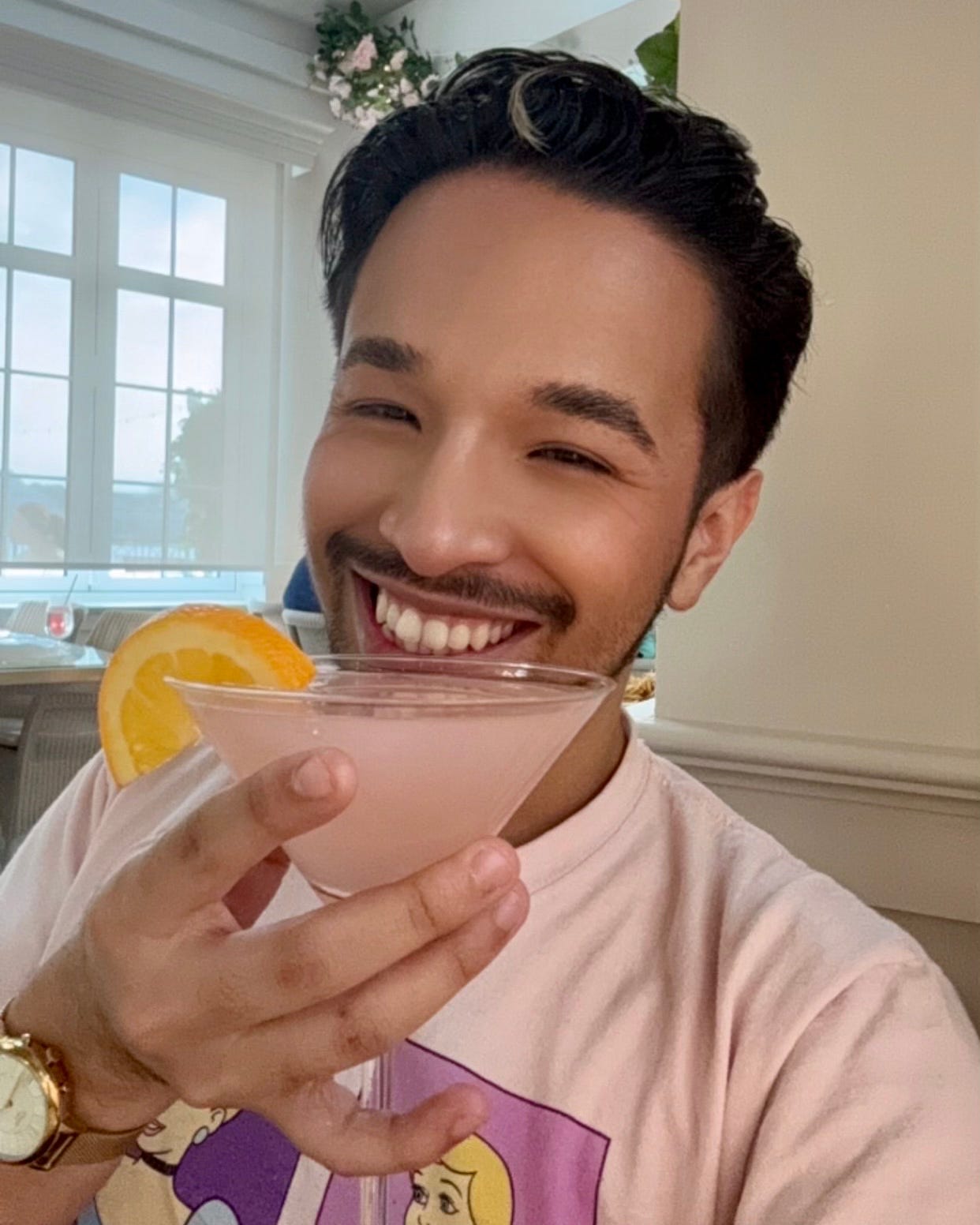 Ditzy Darry smiling and holding a pink cosmopolitan with an orange slice garnish, wearing a pink graphic tee and gold watch. Ditzy Darry smiling and holding a pink cosmopolitan with an orange slice garnish, wearing a pink graphic tee and gold watch.