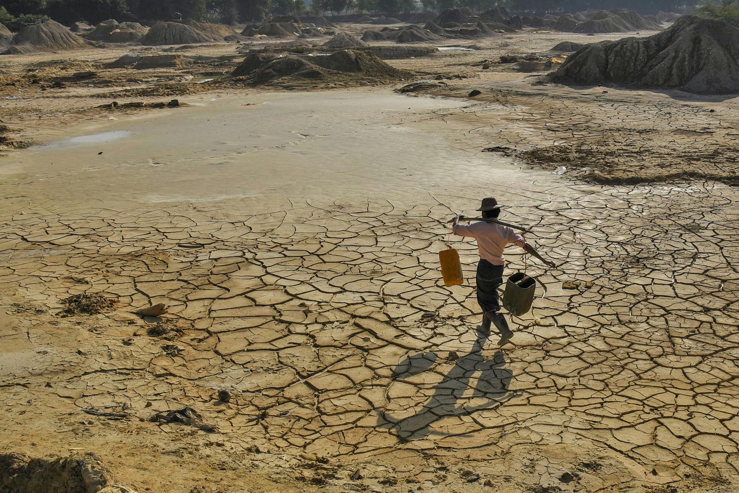 A man carries empty buckets toward a receding pond in Myanmar. A man carries empty buckets toward a receding pond in Myanmar.