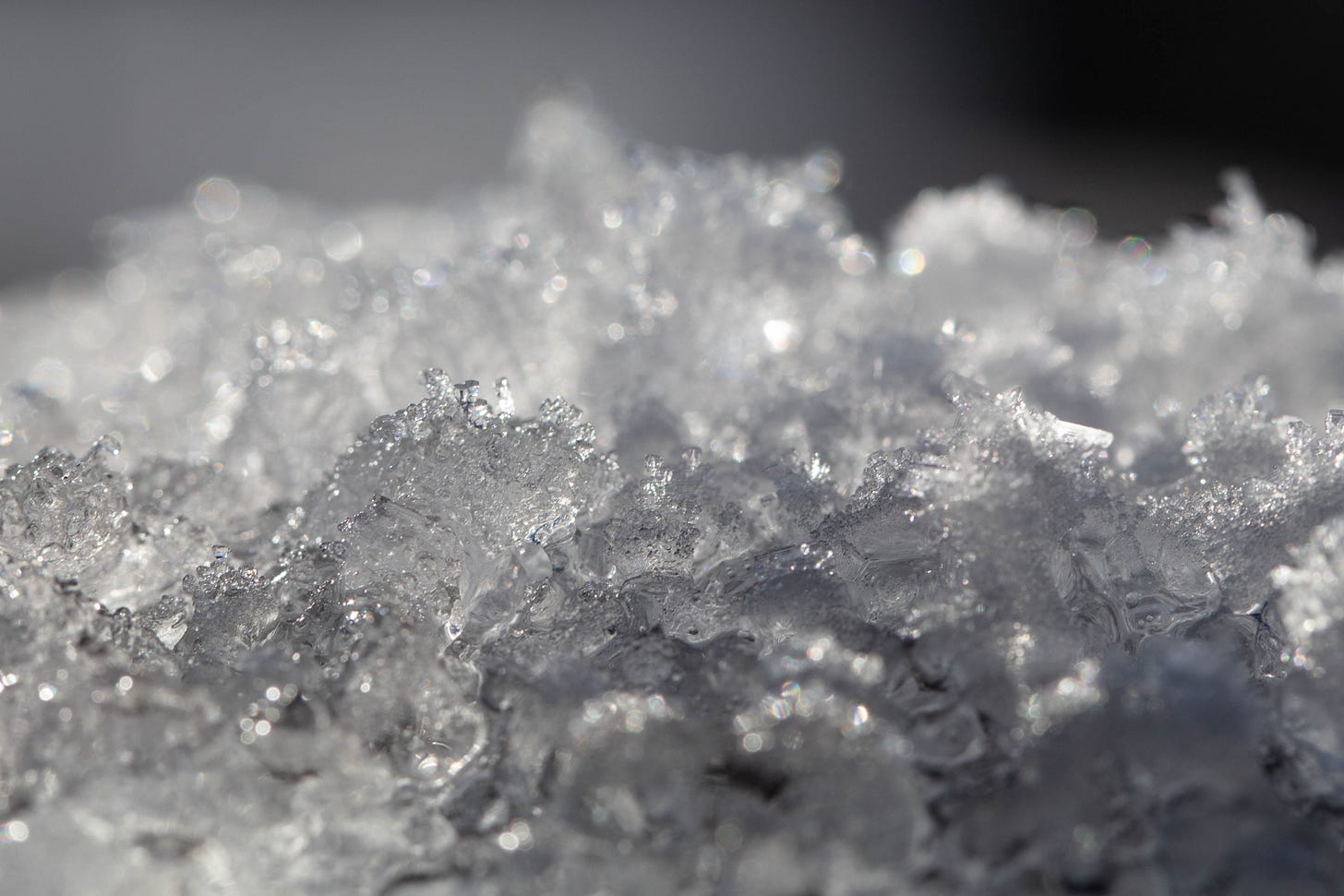 A black-and-white closeup of snow, showing icy crystal shapes in the foreground and fading to soft focus with sparkles in the background
