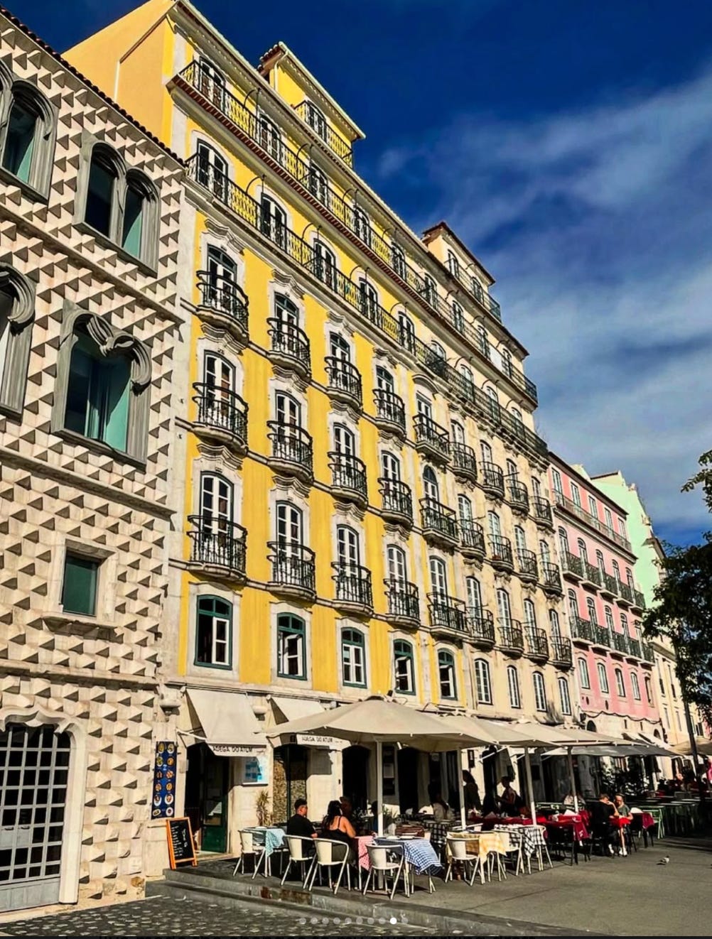 “Yellow riverfront building with street cafés; diamond-pattern façade next door.”