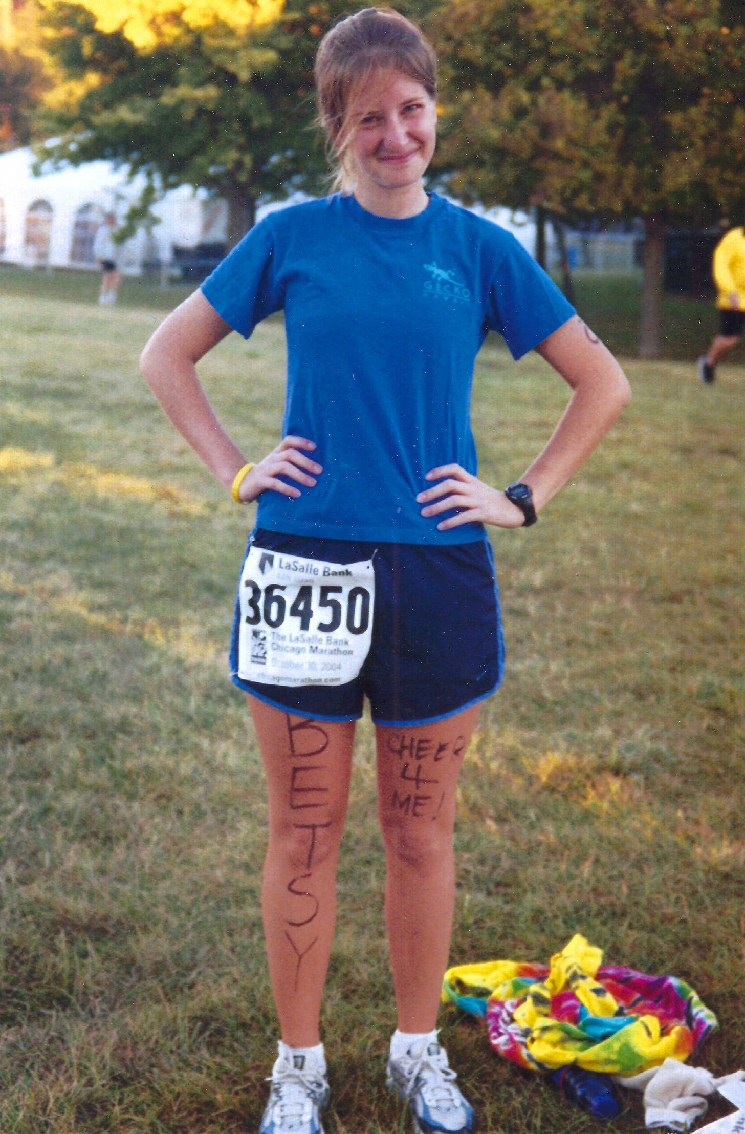 Young woman posing with her hands on her hips before a race. She has a race bib on her shorts and on her legs written in permanent marker are "BETSY" and "Cheer 4 me!"