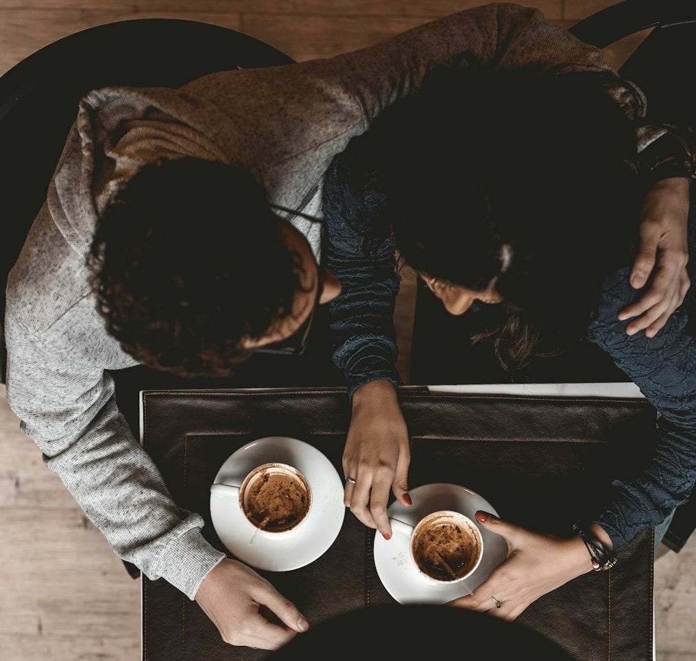 man and woman sitting on floor while holding cups on table