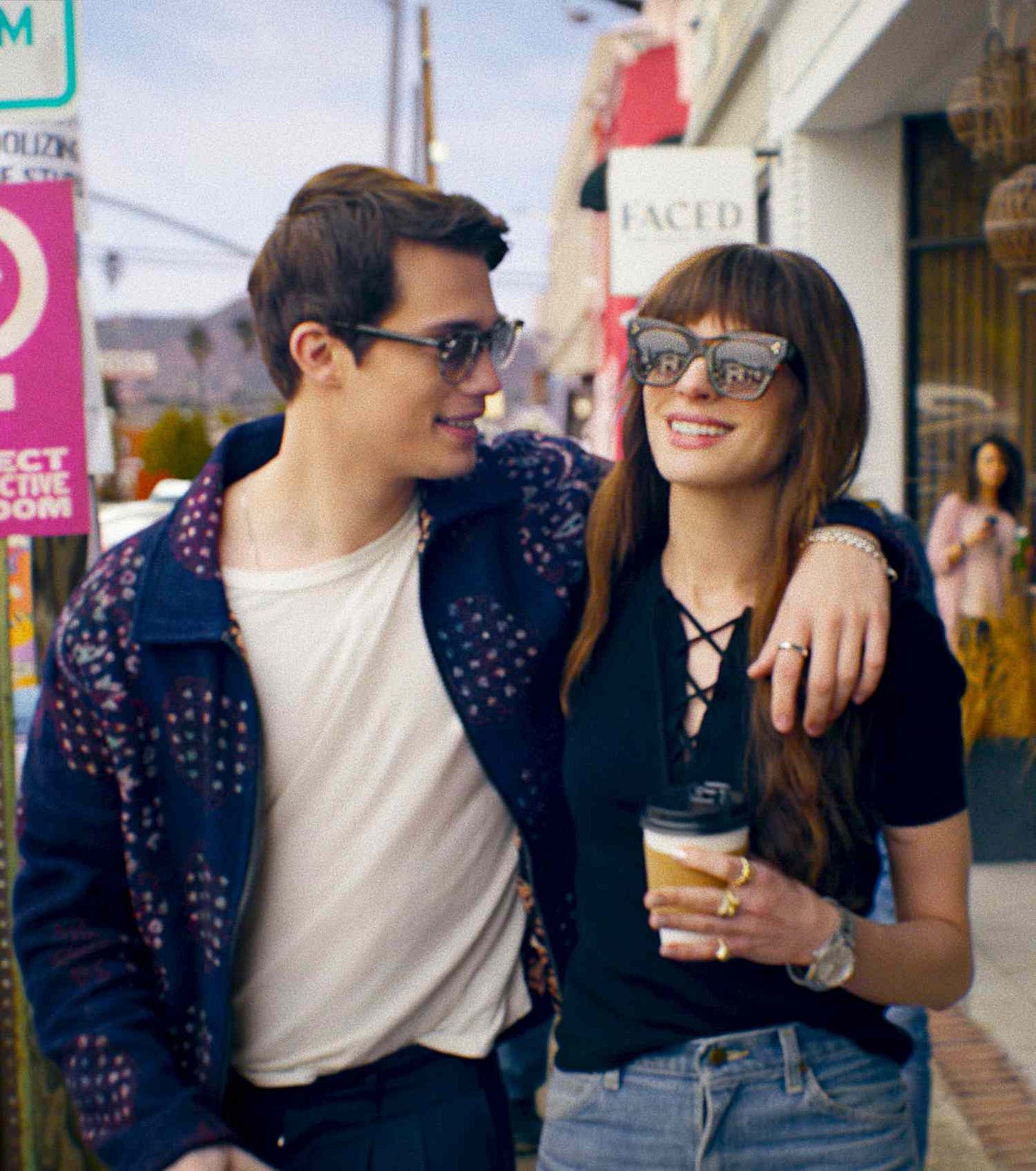 Official image from the film The Idea of You, showing Anne Hathaway and Nicholas Galitzine walking down a road arm in arm and laughing.