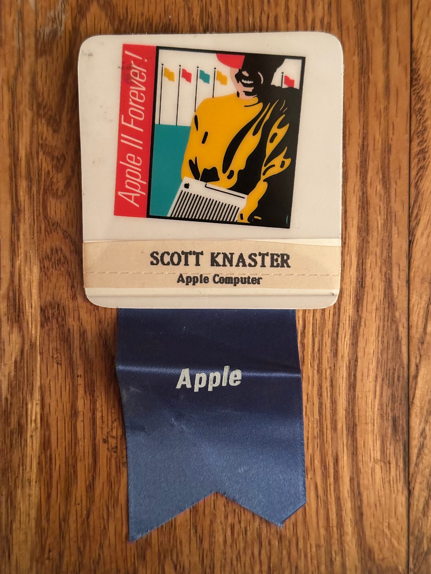Apple II Forever attendee badge, with event logo and blue ribbon reading "Apple" beneath it.