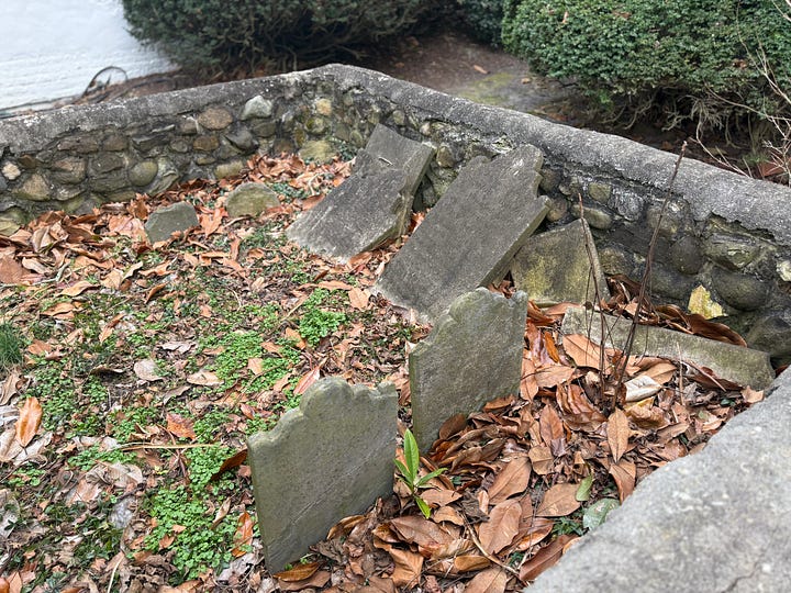 White brick house and cemetery showing old, tilted headstones.