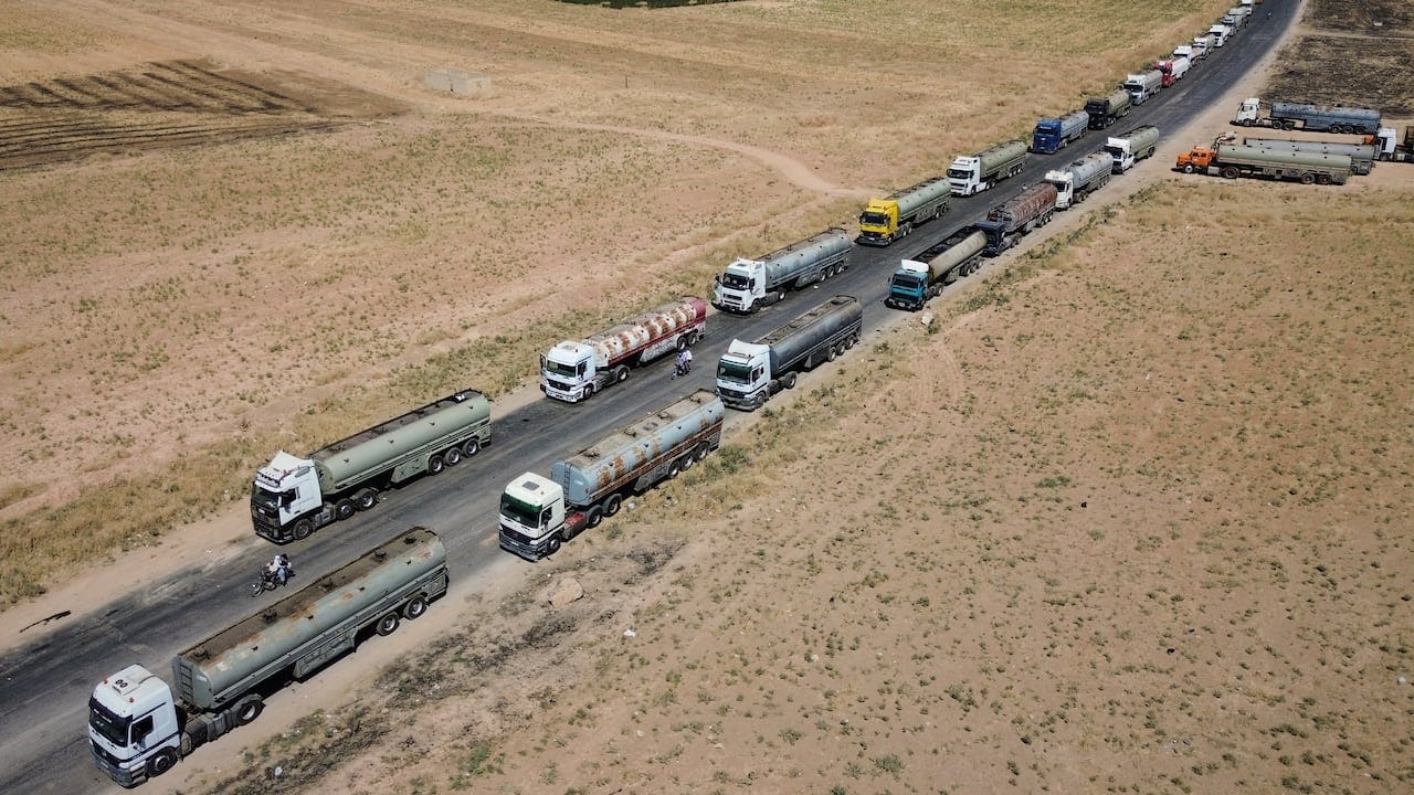 Tractor trailers with oil tanks bumper to bumper on a curved road that stretches into the distance on a mostly brown plain. Tractor trailers with oil tanks bumper to bumper on a curved road that stretches into the distance on a mostly brown plain.