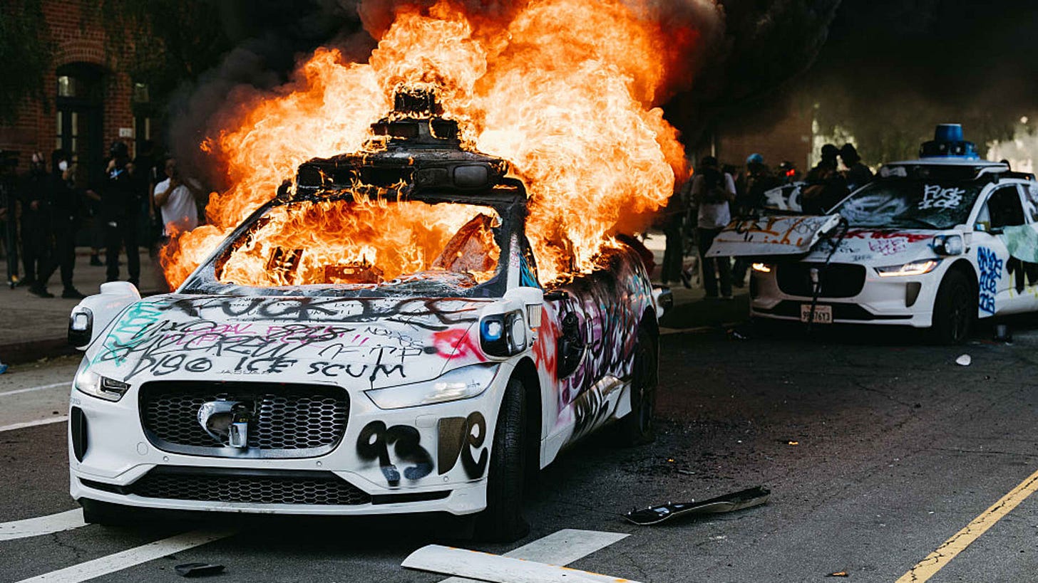 A Waymo car burns in the street as smoke billows during protests in Los Angeles, California, on June 8, 2025. Following a series of aggressive federal immigration operations in Los Angeles, tensions escalated when Immigration and Customs Enforcement (ICE) agents conducted a high-profile raid on a Home Depot location. The raid sparked widespread protests across the city, where demonstrators decried the targeting of immigrant communities and the separation of families. Clashes soon broke out between protester