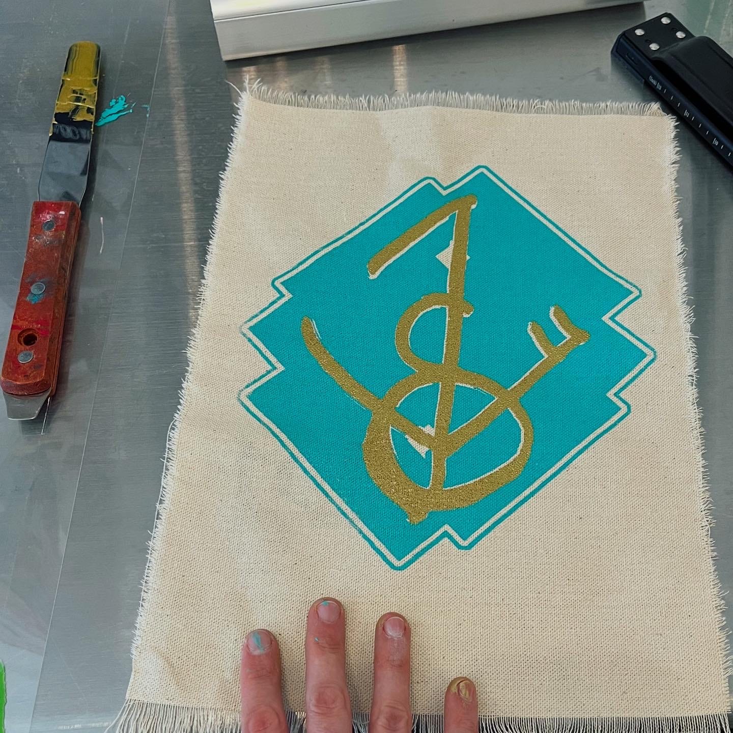 Lark's hand touching a large fabric patch printed with a blue and gold sigil, tools lying nearby
