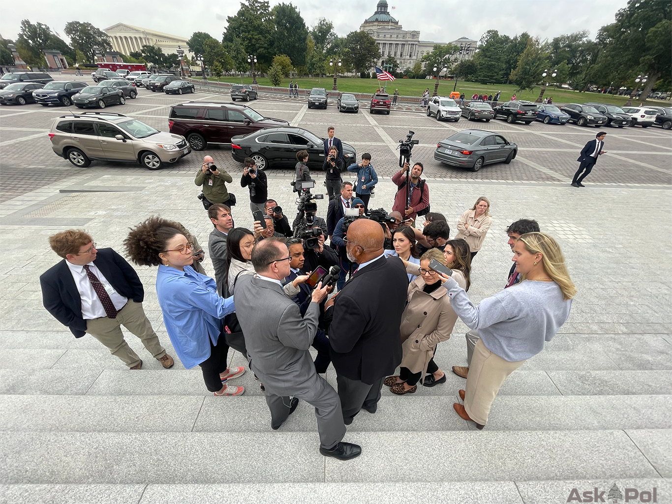 An older Black politician in a suit is surrounded by reporters on the steps of the US Capitol
