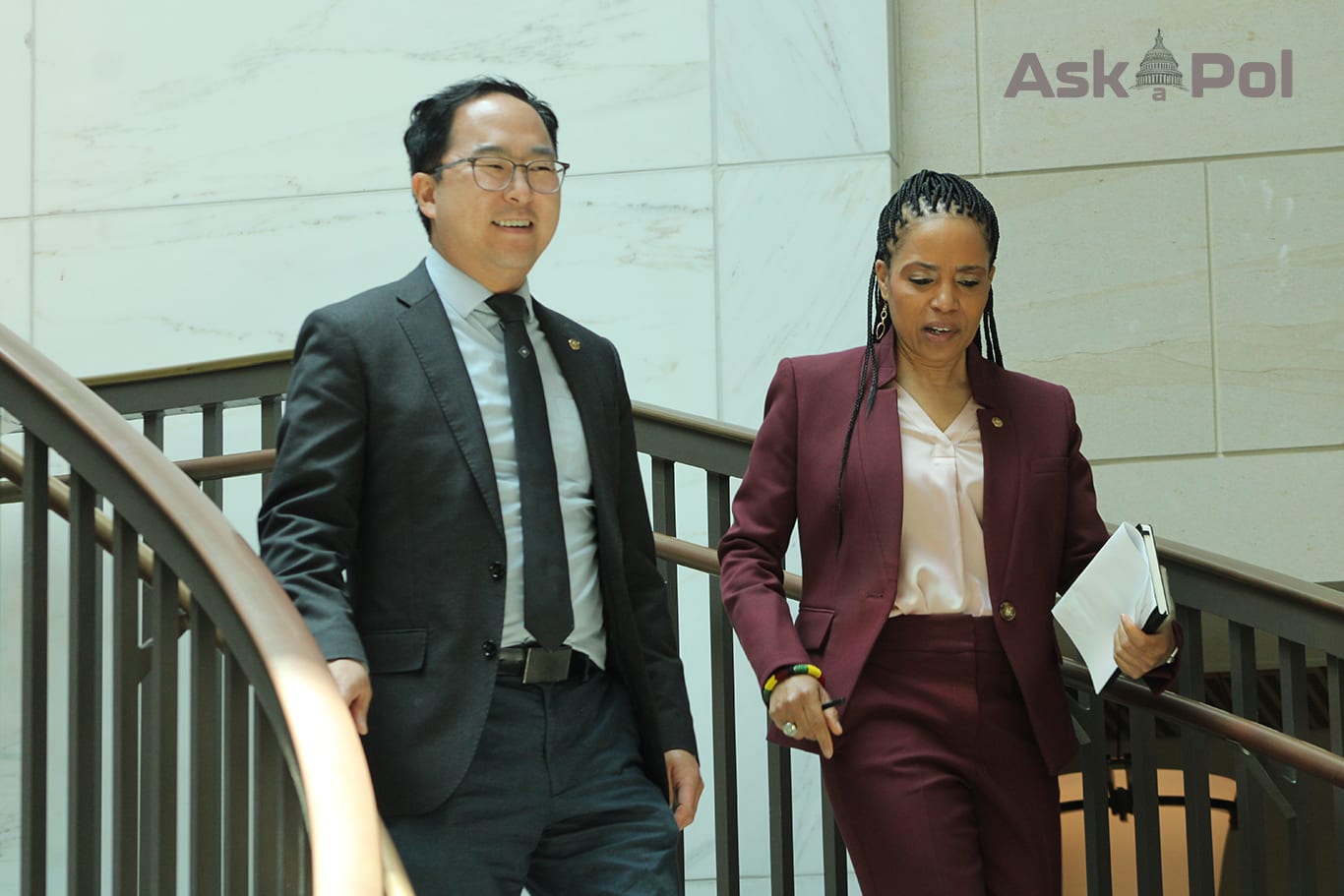 An asian man and Black female in suits walk down a staircase together smiling. Photo: Logan Johnson © Ask a Pol 