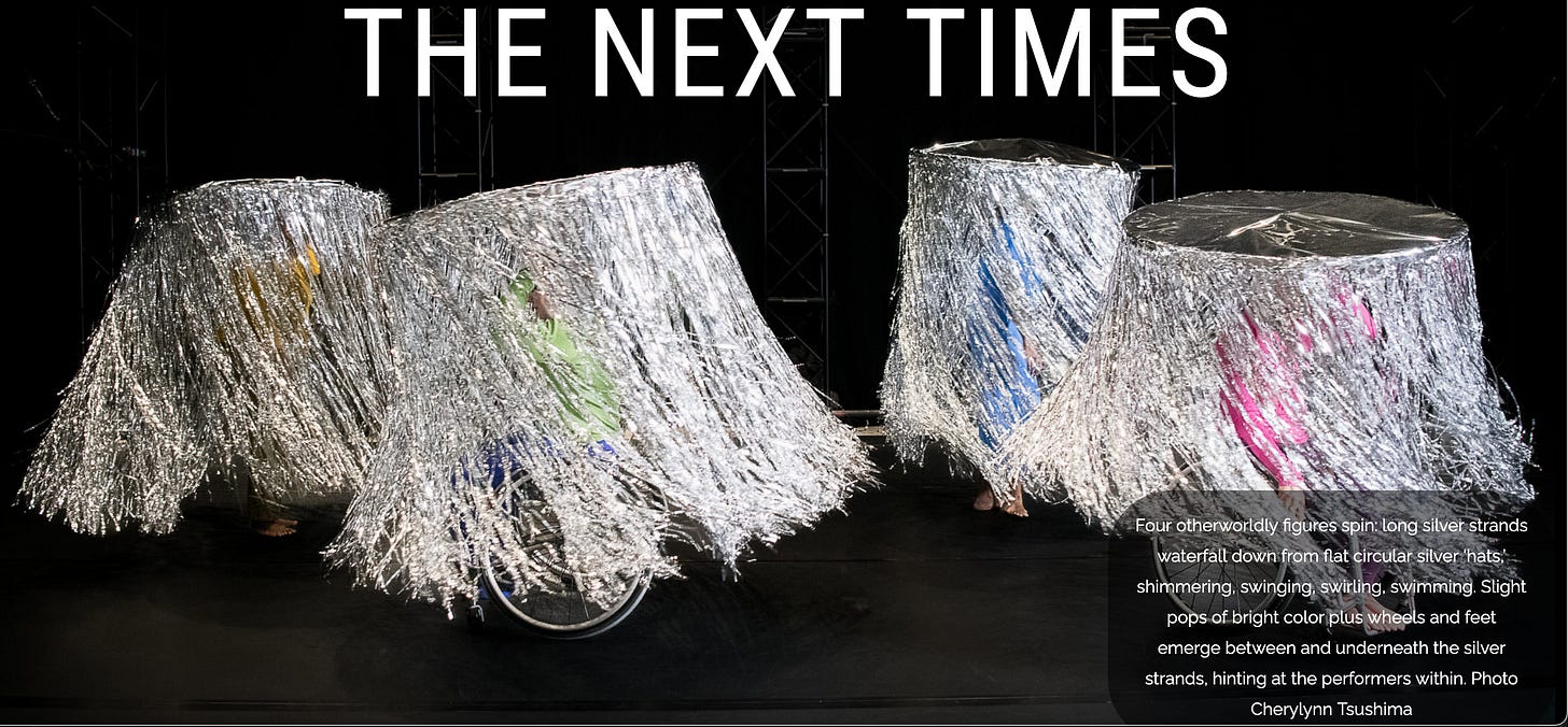 "THE NEXT TIMES Four otherworldly figures spin: long silver strands float down from otherworldly "hats" shimmering, swriling swimming. Wheels and pops of color are visible.