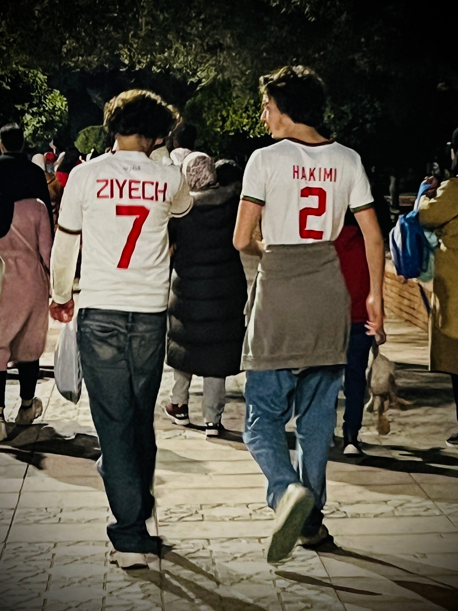 Two people walking through Marrakech wearing Morocco jerseys with "Ziyech 7" and "Hakimi 2"—the most common national team shirts available before the 2022 World Cup.