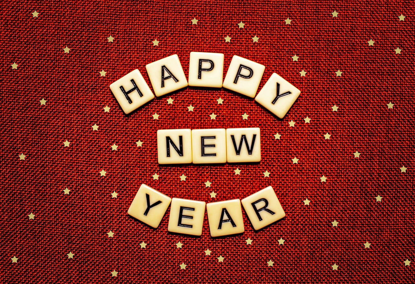 A dark piece of red fabric with tiny gold stars sprinkleld over its surface serves as background for the words Happy New Year, each letter in black on a pale cream-colored tile, with Happy and Year forming the top and bottom curves of a circle and New resting in the middle.