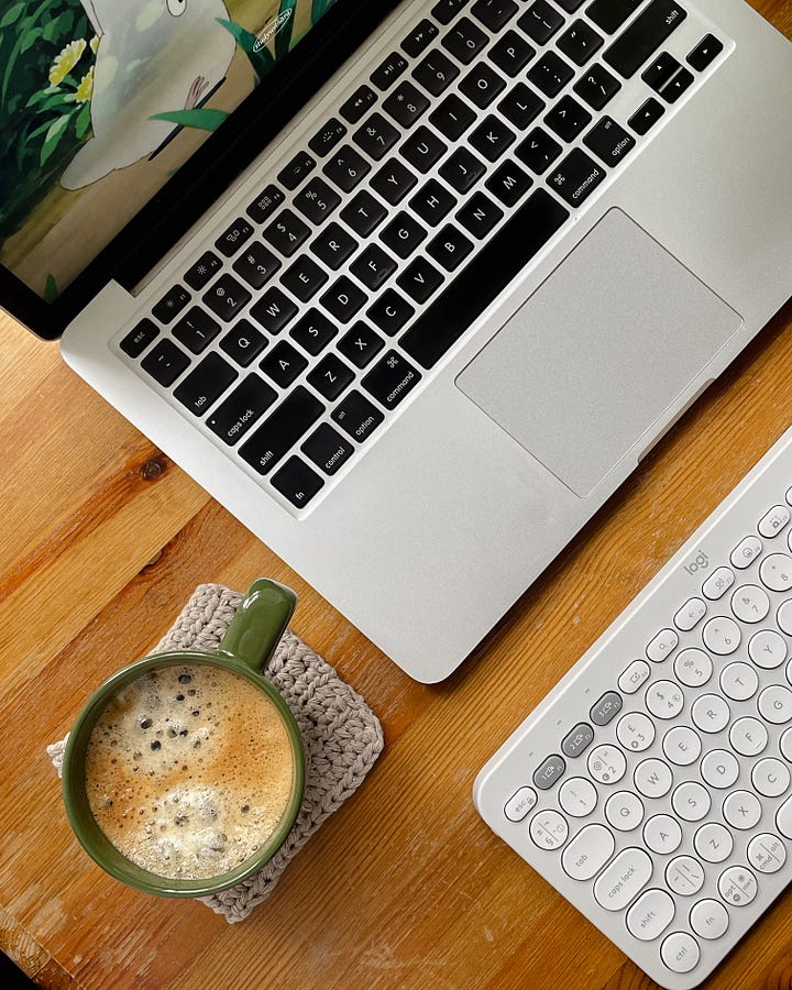 Gallery - Image 1: A close-up of my laptop and cup of coffee on my desk. / Image 2: A close-up of my Muji passport notebook, plant, laptop, and desk accessories.