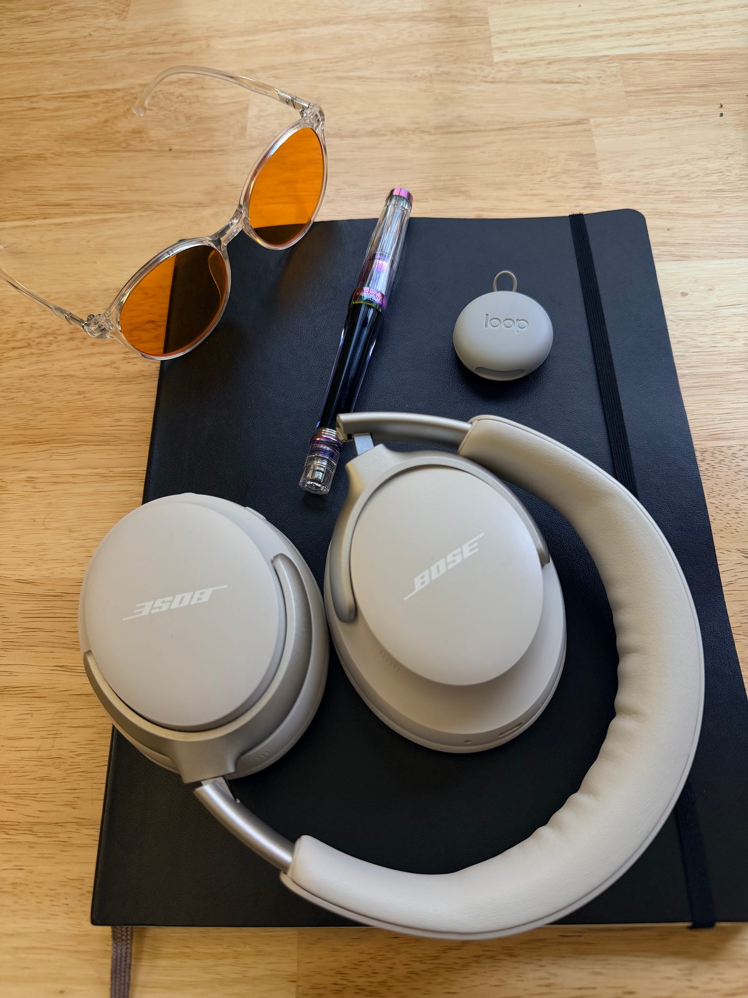 The author's gear. Blue blocking glasses, pen, notebook, headphones, and earplugs.