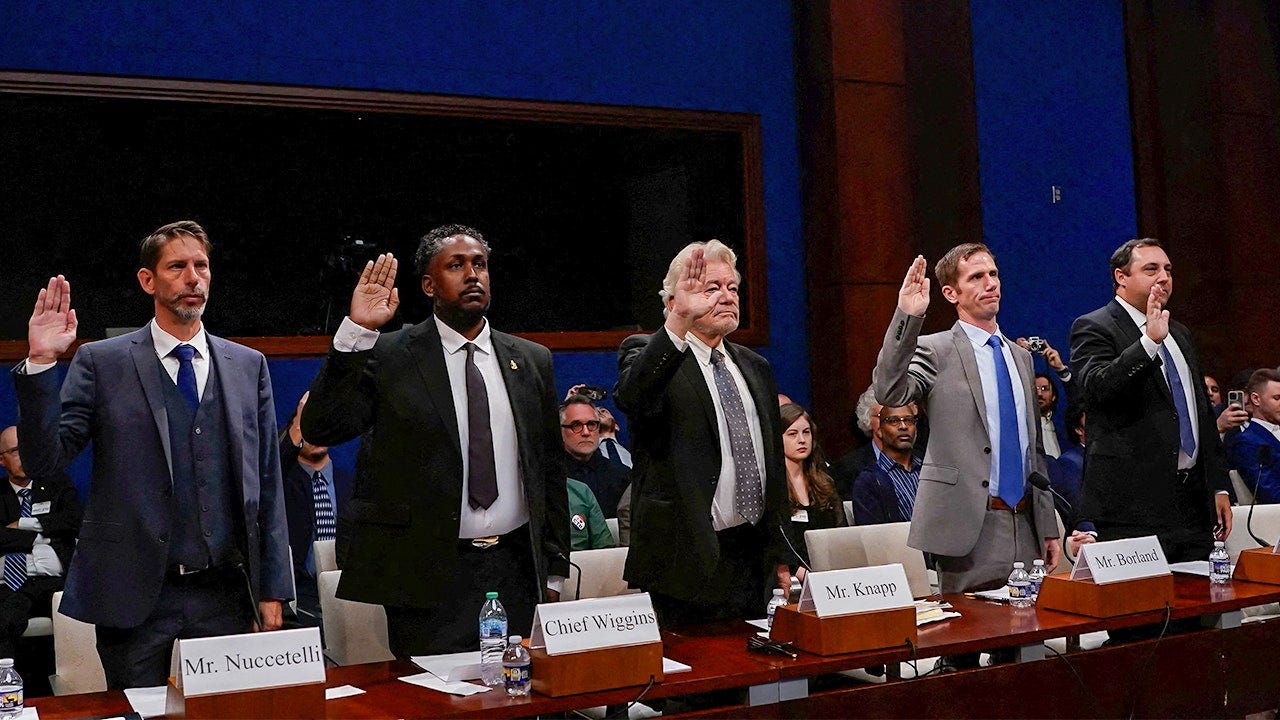 Four male witnesses stand behind a long hearing table inside a congressional chamber, raising their right hands to be sworn in. Nameplates in front of them read Mr. Nuccetelli, Chief Wiggins, Mr. Knapp and Mr. Borland. Seated audience members and blue-paneled walls are visible in the background. Four male witnesses stand behind a long hearing table inside a congressional chamber, raising their right hands to be sworn in. Nameplates in front of them read Mr. Nuccetelli, Chief Wiggins, Mr. Knapp and Mr. Borland. Seated audience members and blue-paneled walls are visible in the background.
