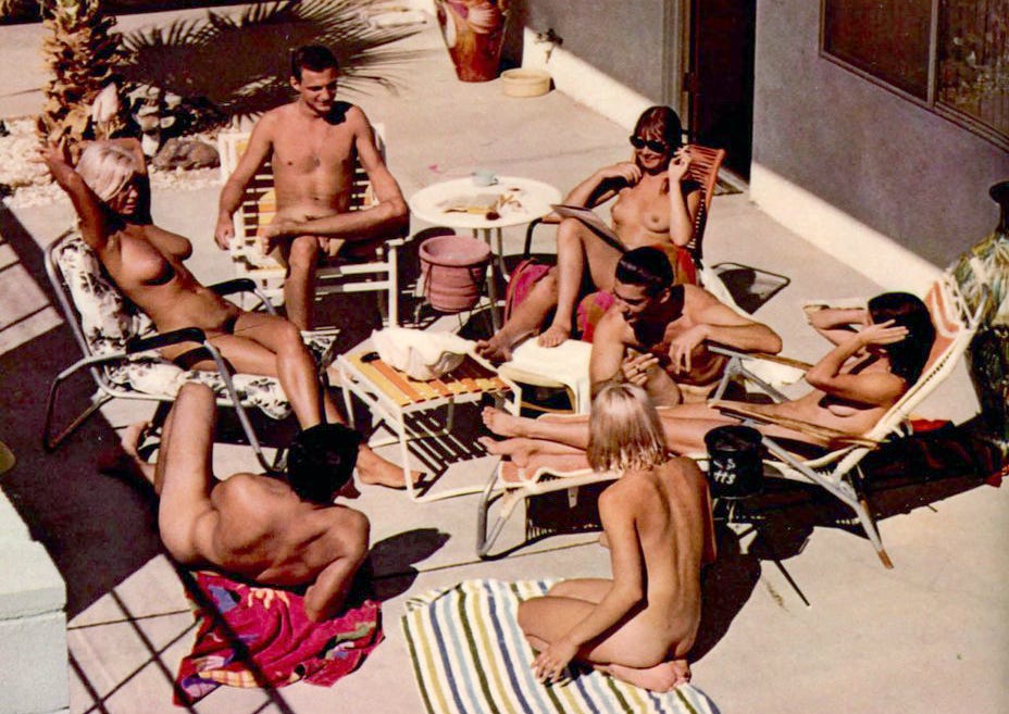 Nude men and women relaxing together on a sunny patio.