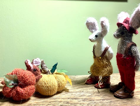 Two rabbits looking at two pumpkins, and a tiny rabbit head poking out. The bigger rabbits look shocked.