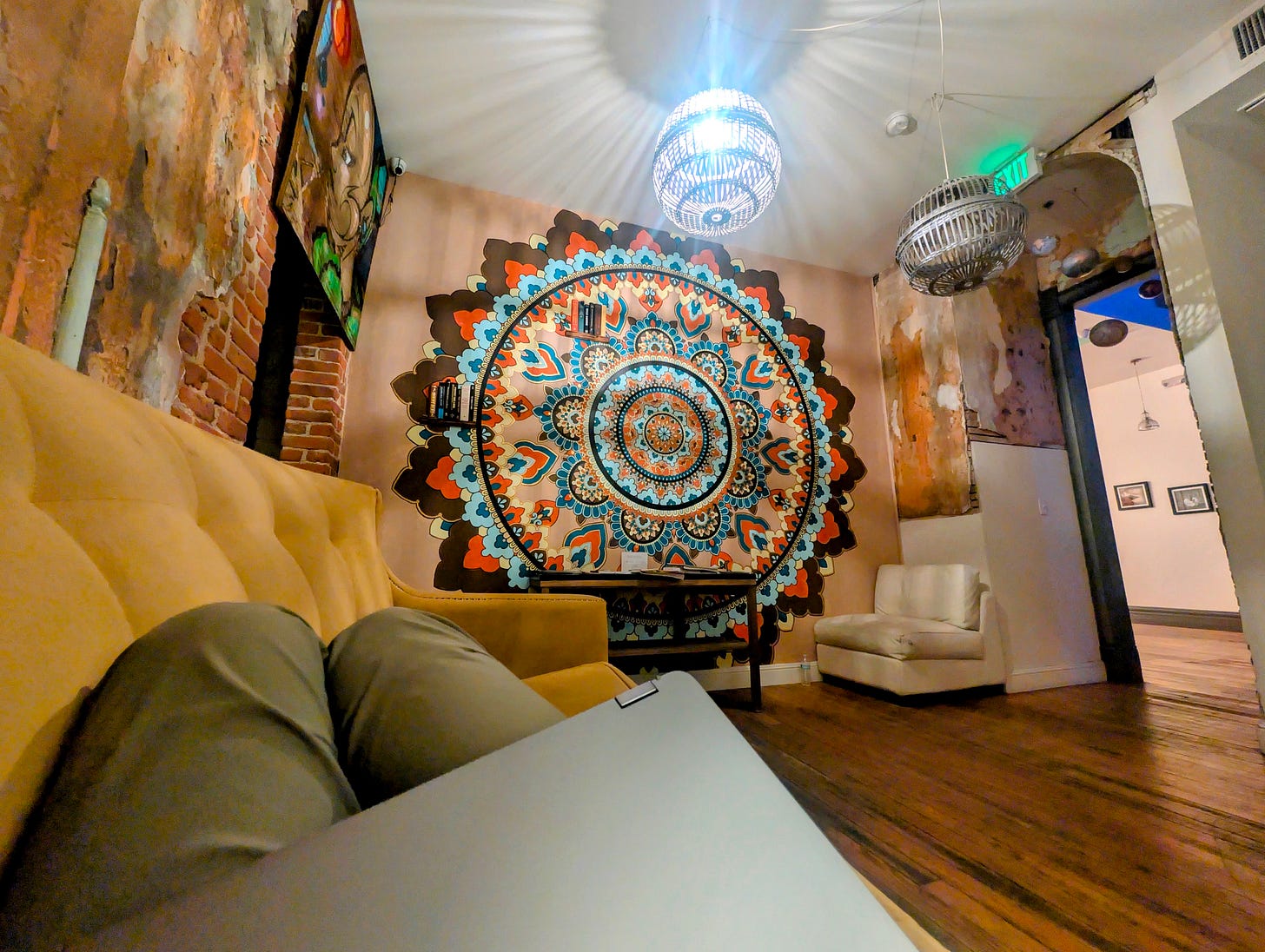 Colorful mandala tapestry and rustic exposed-brick walls inside Hostel Fish in Denver, with couches and soft lighting setting a bohemian tone. Colorful mandala tapestry and rustic exposed-brick walls inside Hostel Fish in Denver, with couches and soft lighting setting a bohemian tone.