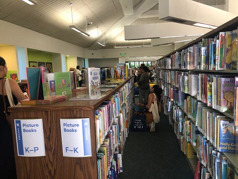 Adults and children in a public library borwworing, browsing, returning  books 