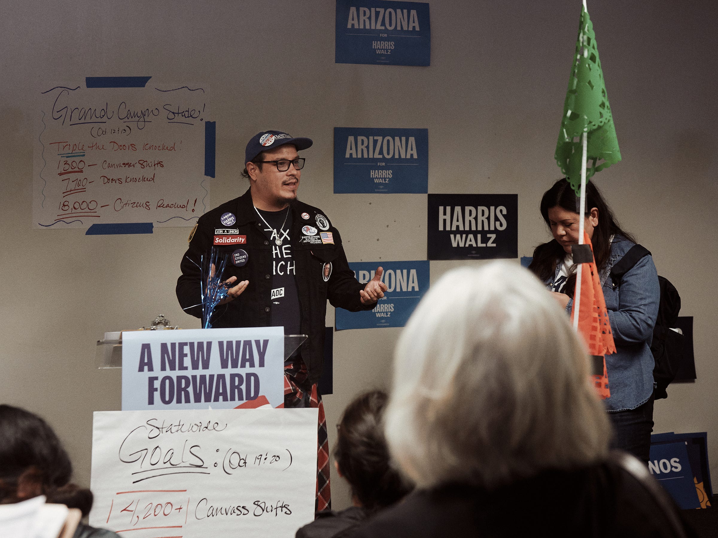 A man stands in front of Harris Walz campaign posters on a podium to train canvassing volunteers for their day ahead. Taken by Los Angeles portrait and documentary photographer Afonso Salcedo.
