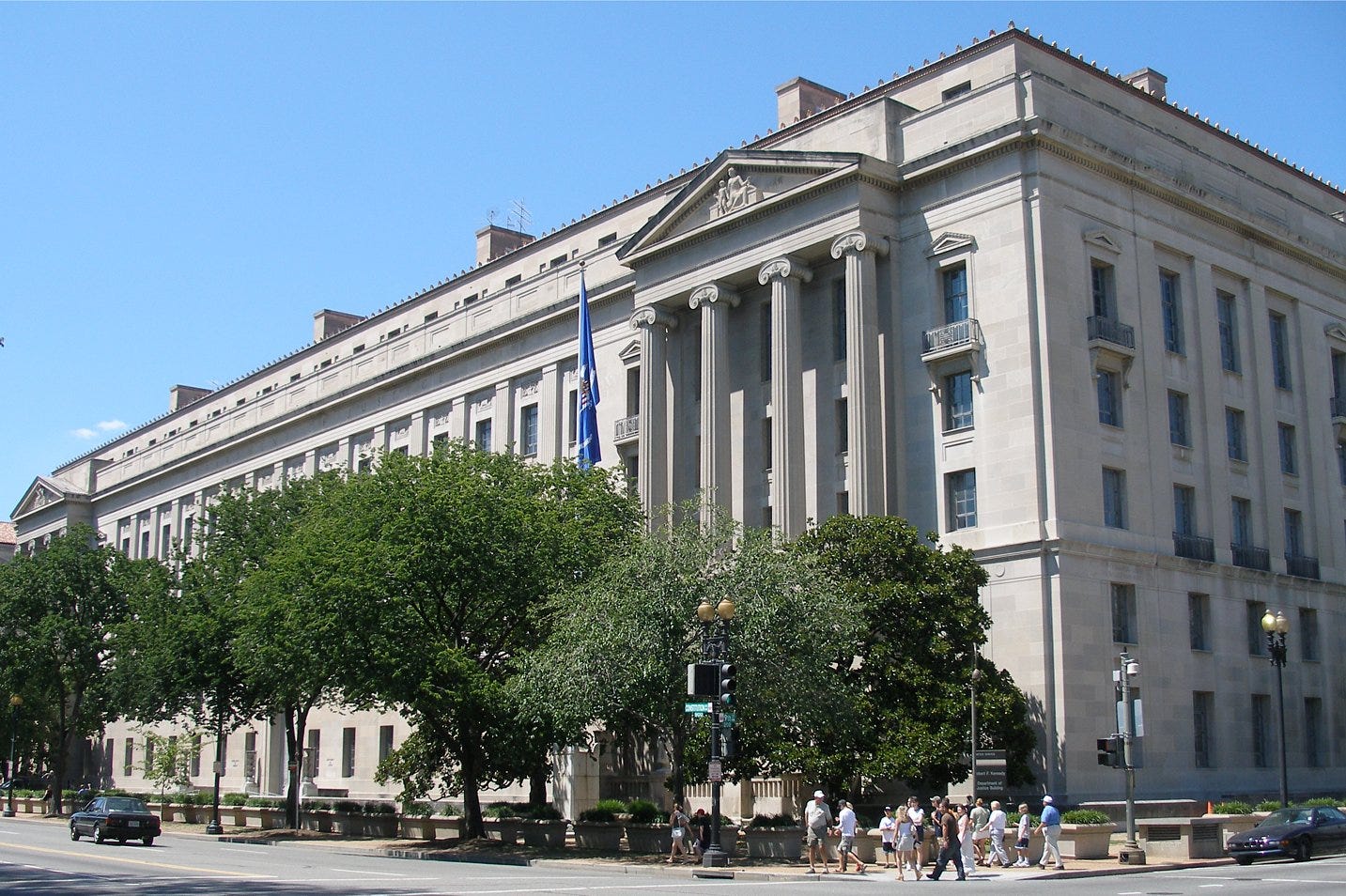 US Dept. of Justice building with car on road and people in crosswalk