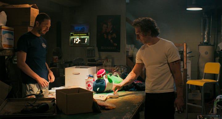 Richie and Carm talk in Richie's basement while in the background a neon sign ticks off time and temperature