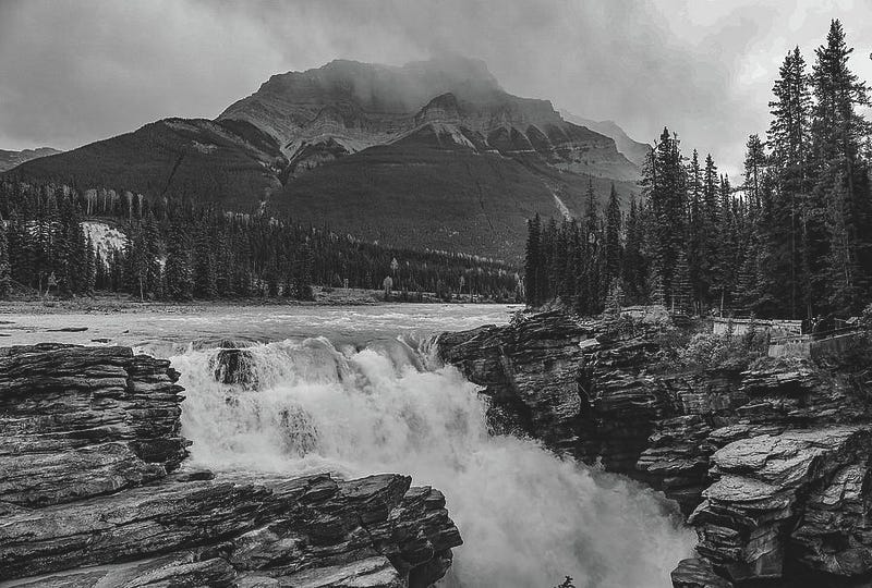 Black and white photograph of Athabasca Falls, with rushing water cascading over rocky cliffs and mist rising from the gorge.