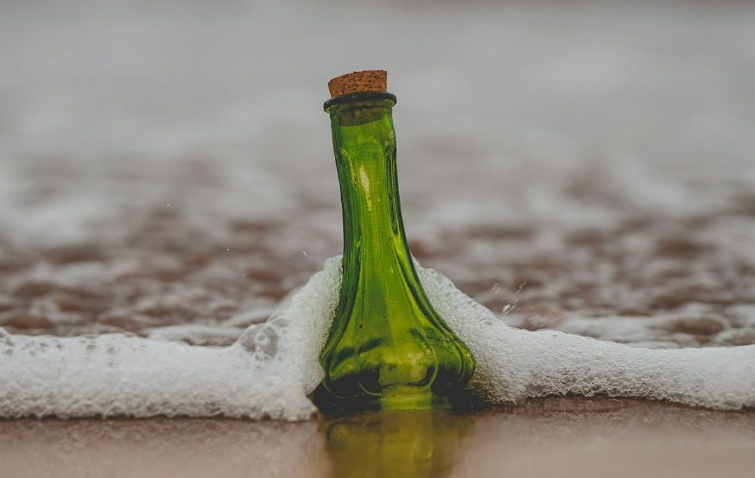 green glass bottle with cork lid on shore green glass bottle with cork lid on shore