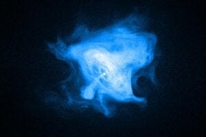 In the Crab Nebula, a rapidly spinning neutron star, or pulsar (white dot near center), drives the activity seen by Chandra. Its inner X-ray ring marks a shock wave where the pulsar wind meets the surrounding nebula. Energetic matter and antimatter flow outward, forming jets from the poles and bright outer rings, while magnetic forces sculpt the nebula’s outer fingers, loops, and bays.