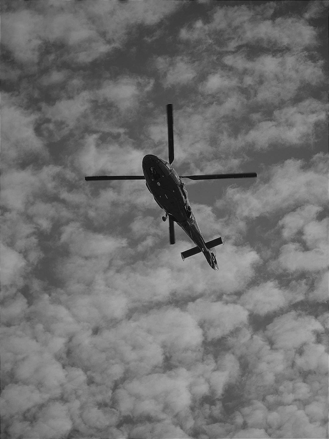 a helicopter flying through a cloudy blue sky