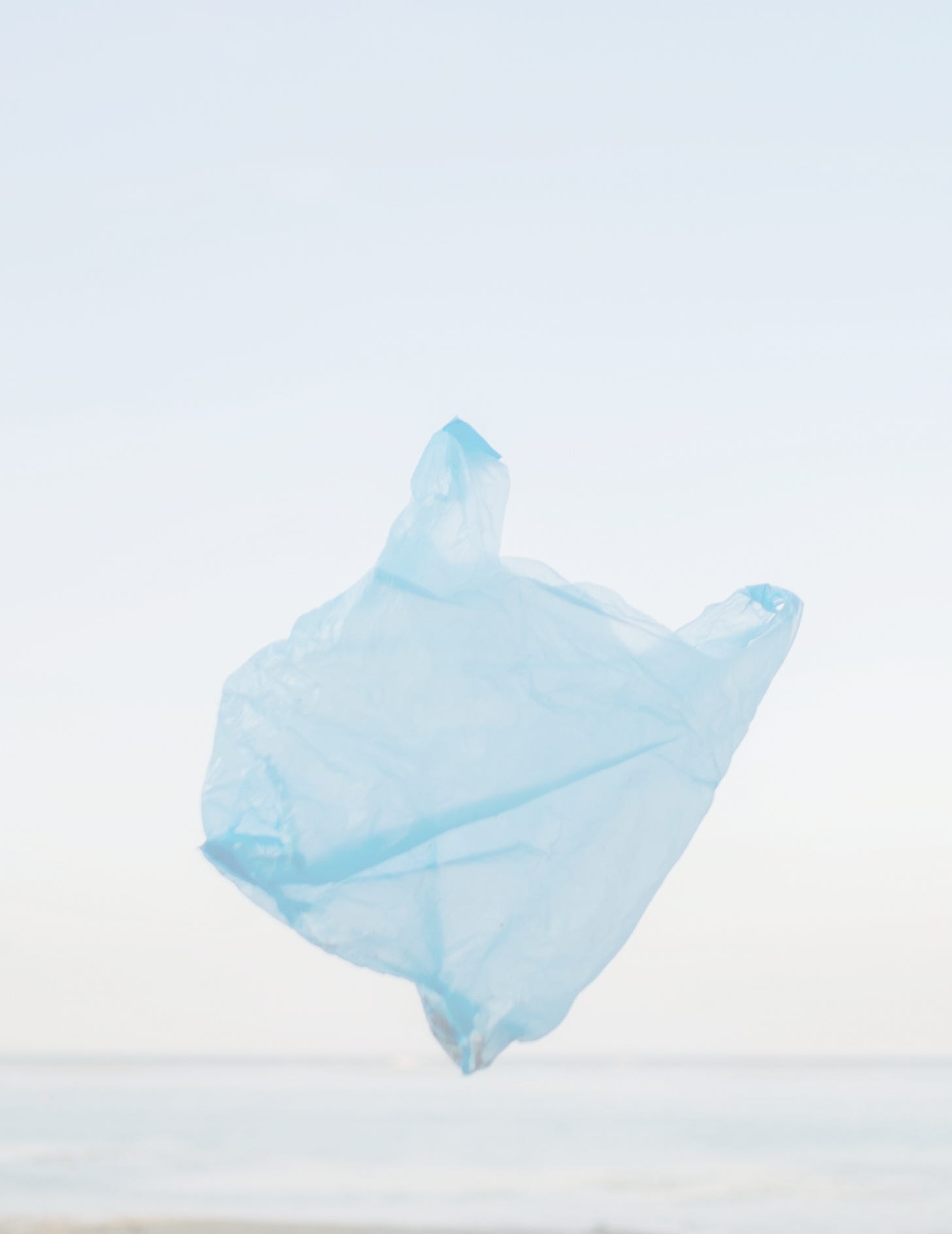 A blue grocery bag floating in the foreground of a beach during sunset.