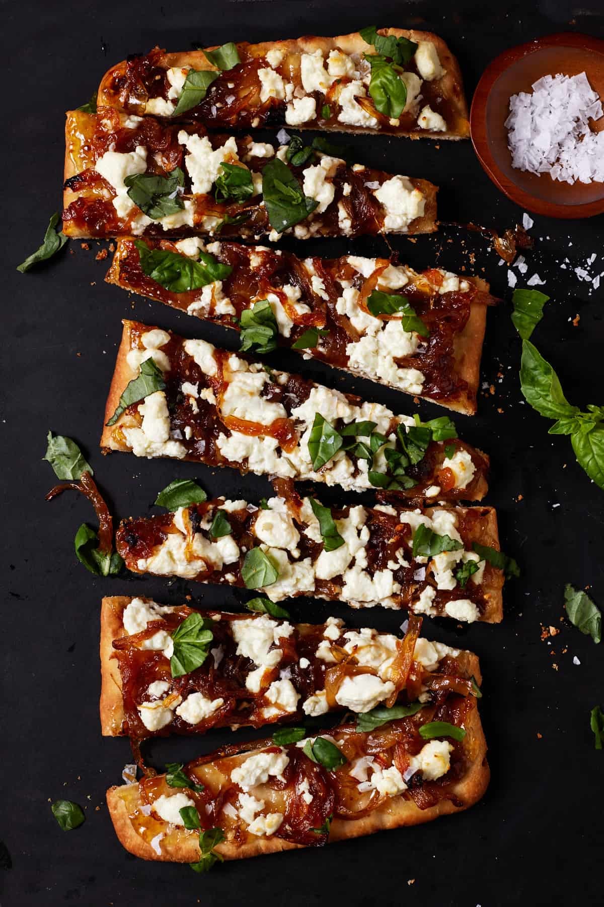 Pieces of goat cheese pizza on a black cutting board with a bowl of sea salt. Pieces of goat cheese pizza on a black cutting board with a bowl of sea salt.