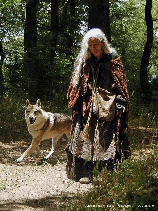 This may contain: an old woman walking with a wolf in the woods