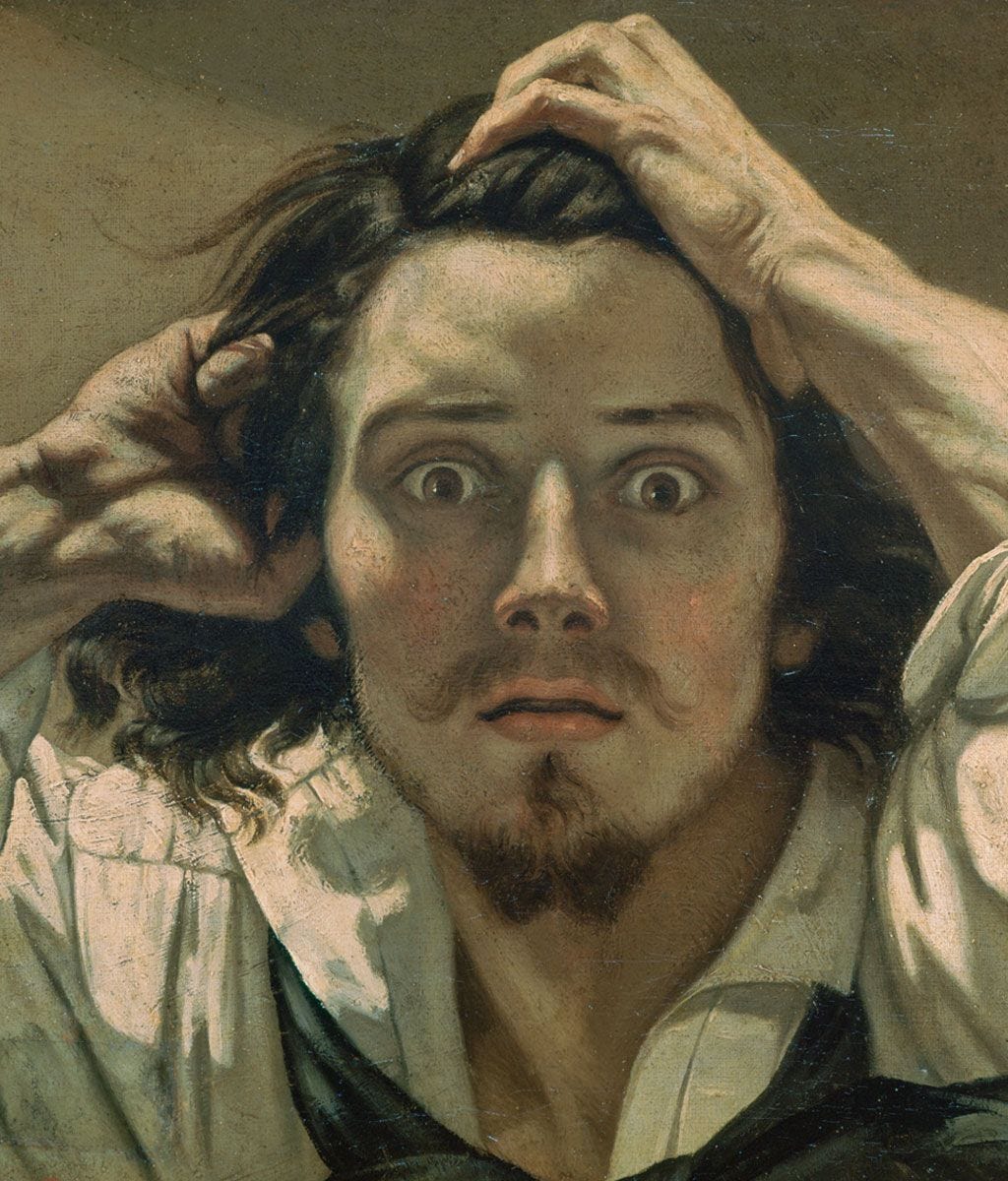 A man with wide eyes and disheveled hair holds his head with both hands, expressing shock or surprise, against a plain background.