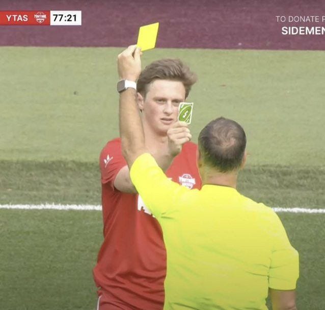 This may contain: two men on a field with one holding up a yellow card and the other wearing a red shirt