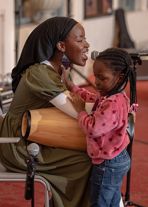 Teledalase singing and playing her hand drum with her child at Delaware Music Network Open Mic.