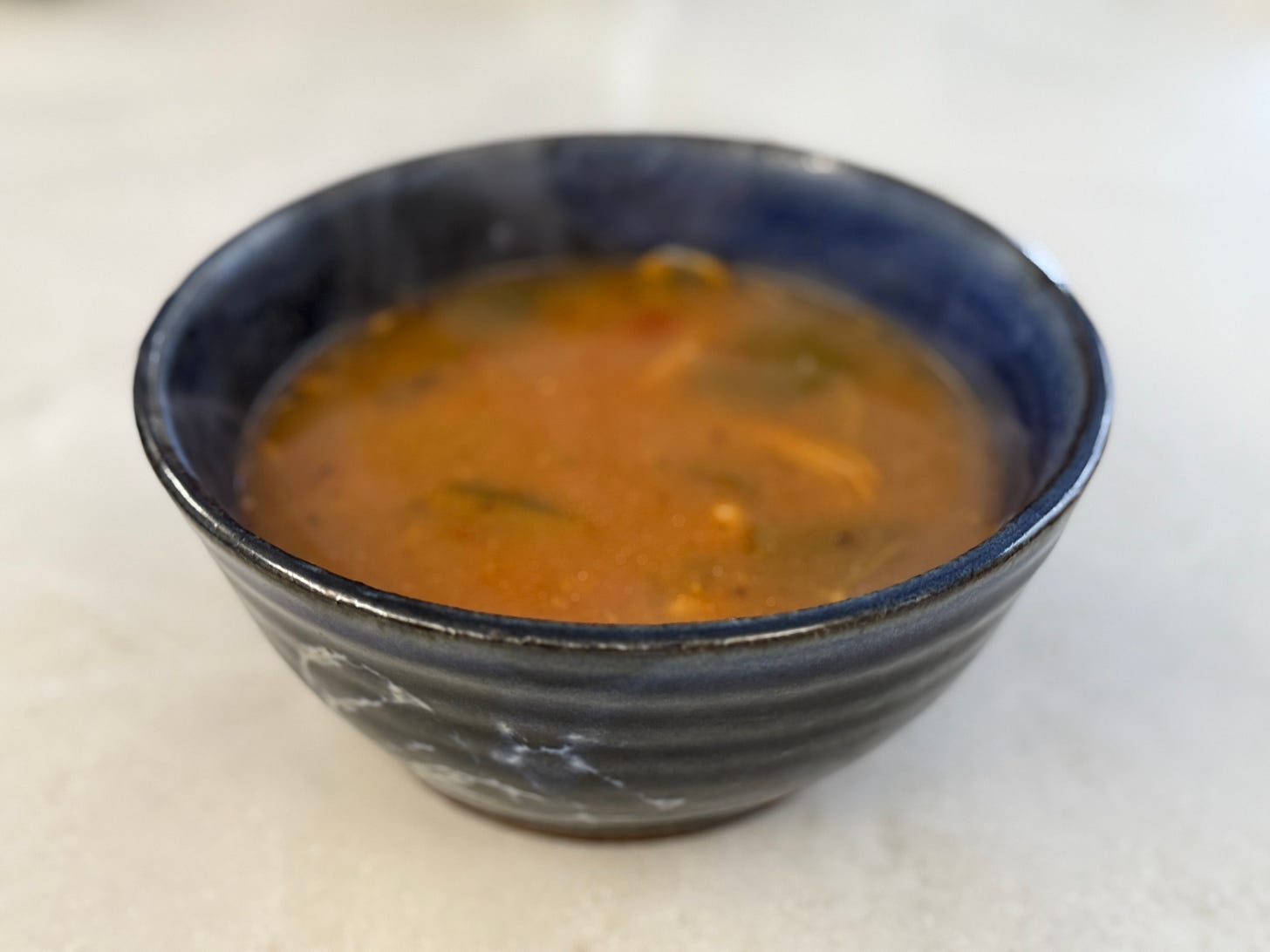 A simple blue bowl of warm soup on a quiet table, with the background softly blurred—capturing a calm pause from grind mode.