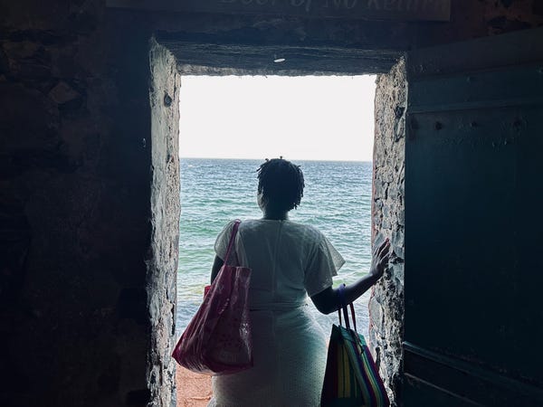 A woman with her back to the camera looks out of a door onto the sea