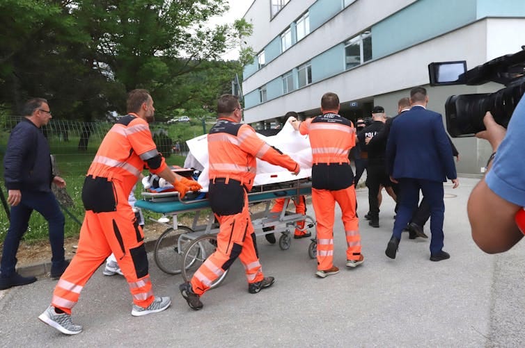 Paramedics wheel a stretcher into a hospital, holding up sheets to cover the person on the stretcher.