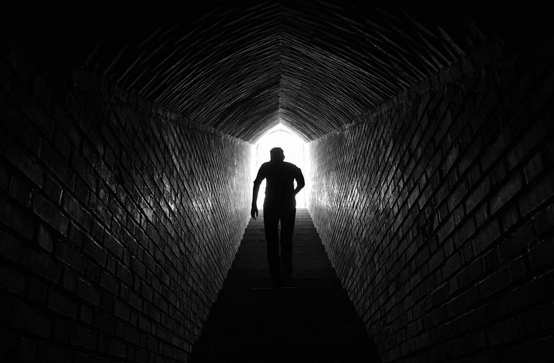 A man walks up the stairs from an underground tunnel approaching the incoming light.